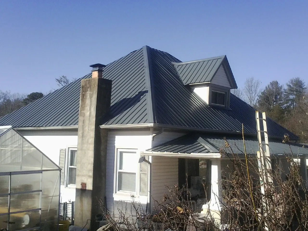 Dark blue standing seam metal roof on a white farmhouse with dormer — Slate & Tile Roof Repair by Roofing Brothers in Wilburton