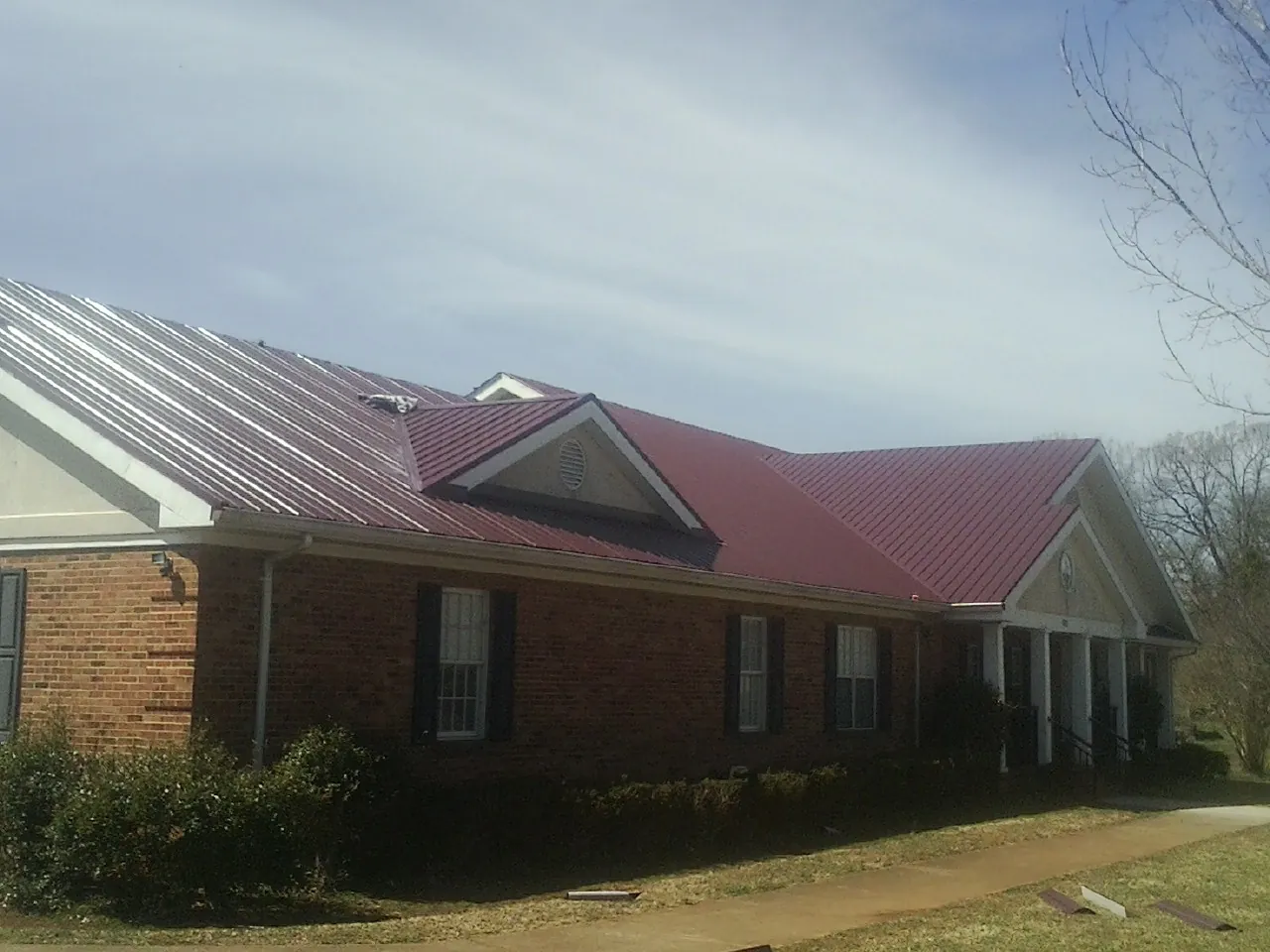 Red metal roof with gabled entries on a long brick building, from a Hail Damage Roof Repair job in Wilburton