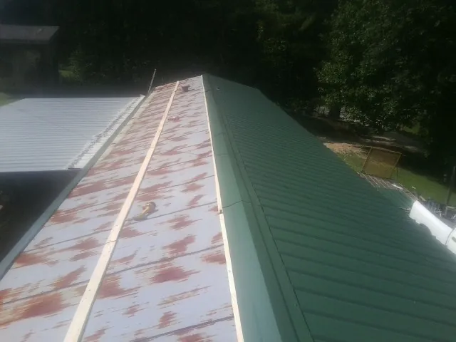 Old rusted panels beside newly installed green metal roofing — Wind Damage Roof Repair by Roofing Brothers in Wilburton