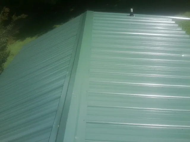 New green metal panels meeting at the ridge of a roof — Flat Roof Repair work by our crew in Wilburton