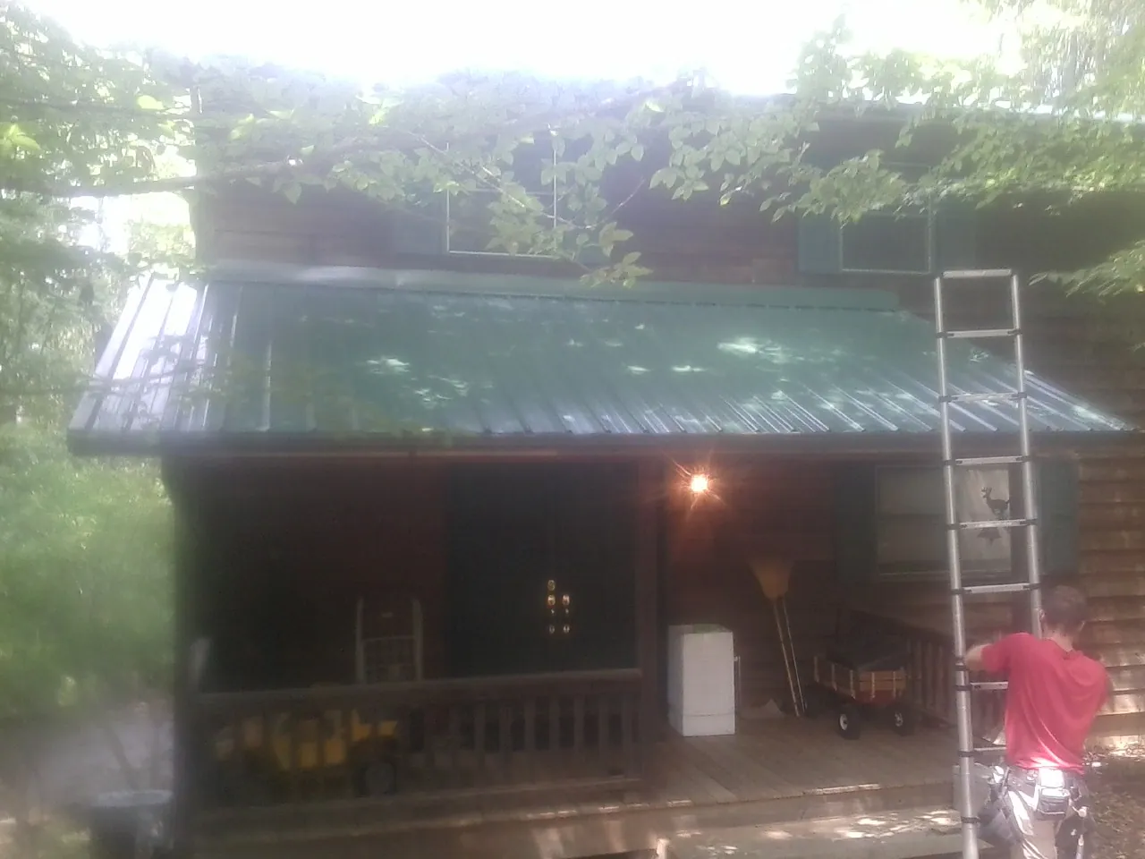 Worker on a ladder at the green porch roof of a wooded cabin in Wilburton