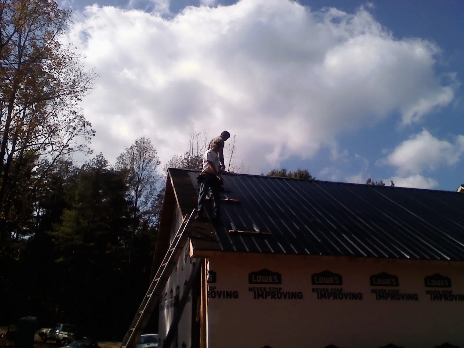 Roofer fastening dark metal panels high against a cloudy sky, from a Roof Inspection job in Wilburton