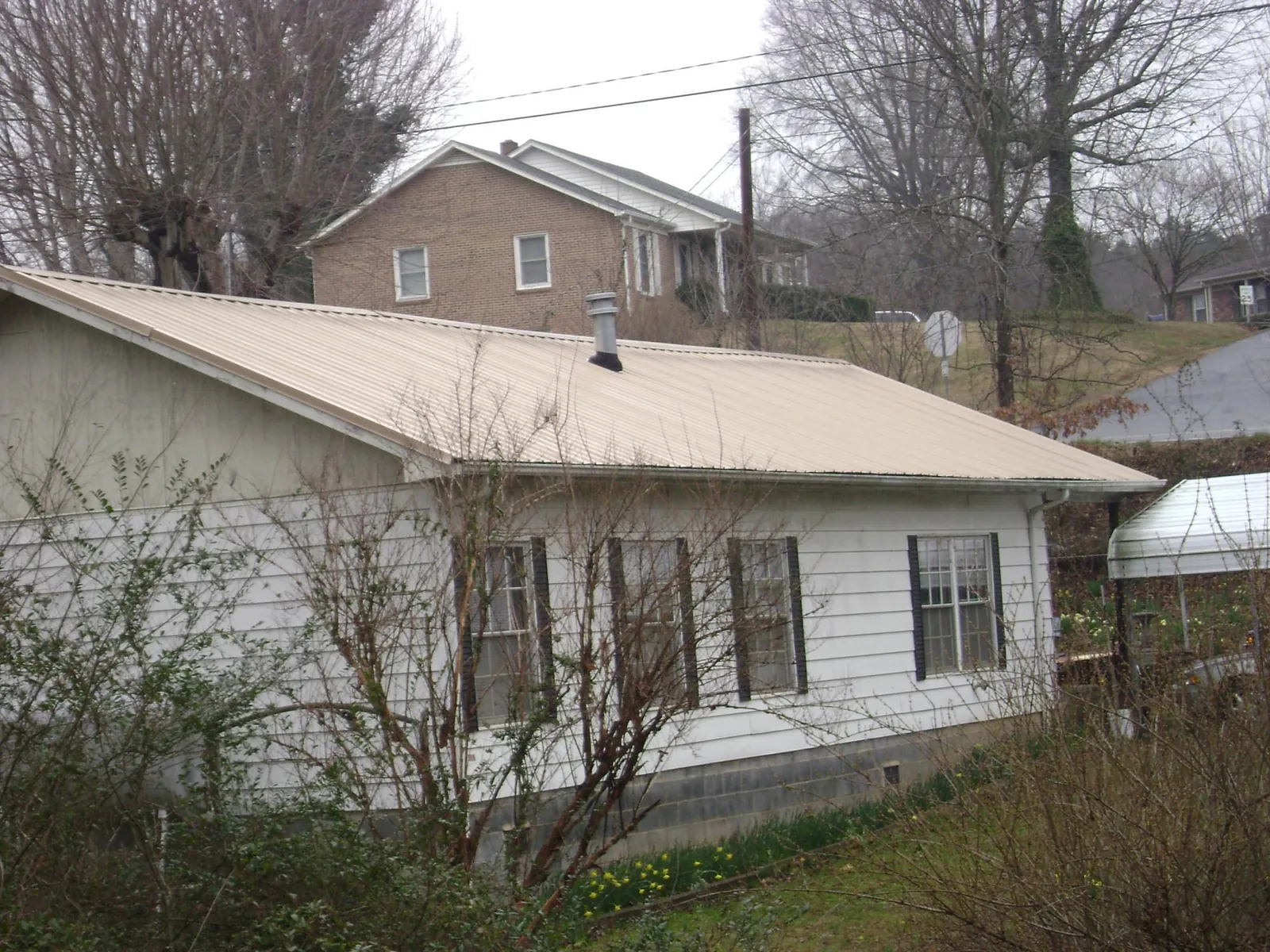 Tan metal roof on a white sided house set into a hillside — Commercial Roofing by Roofing Brothers in Wilburton