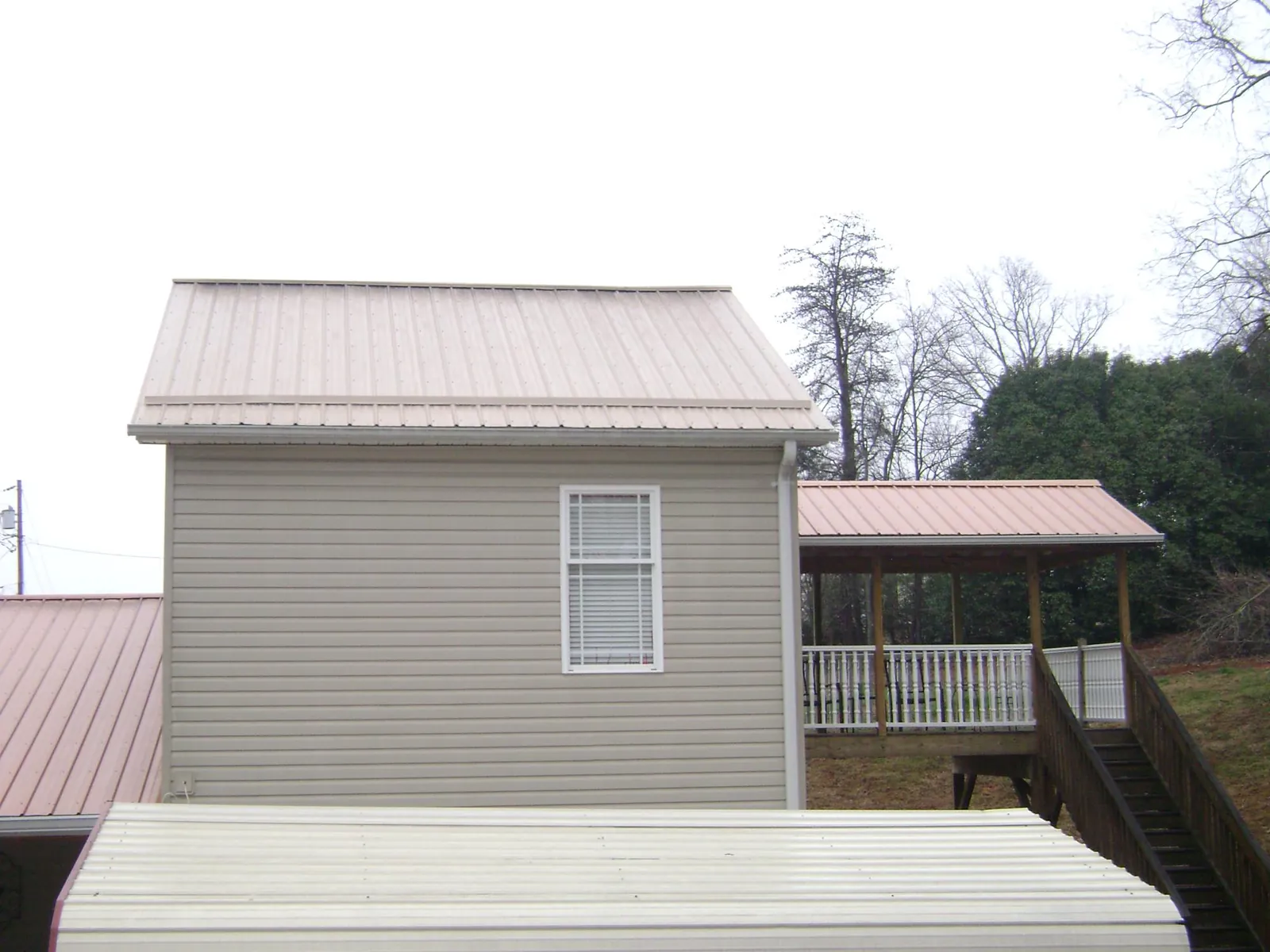 Tan metal roofs on a two story addition and attached porch, from a Roof Replacement job in Wilburton