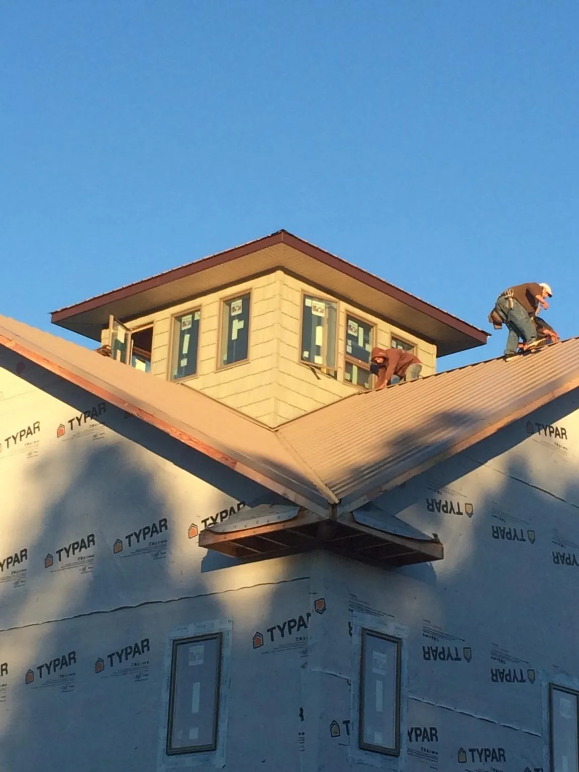 Roofers working around a rooftop cupola on a new metal roof at sunset — Roof Waterproofing in Wilburton by Roofing Brothers